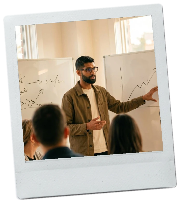 Polaroid of Amit at a whiteboard, drawing a chart for a room of people